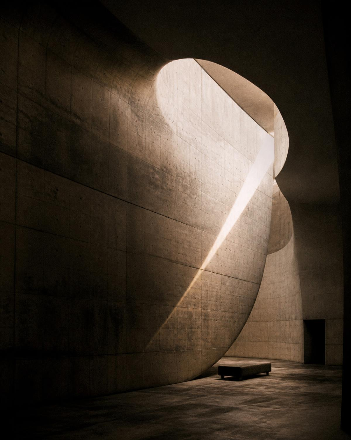 Curved raw concrete interior lit by a single shaft of daylight